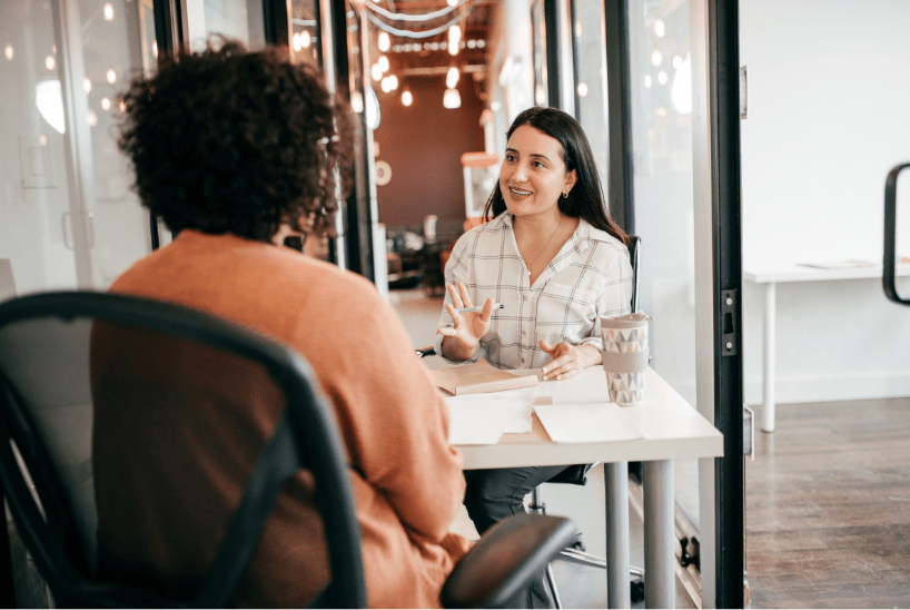 Two people talking across a table in a bright office